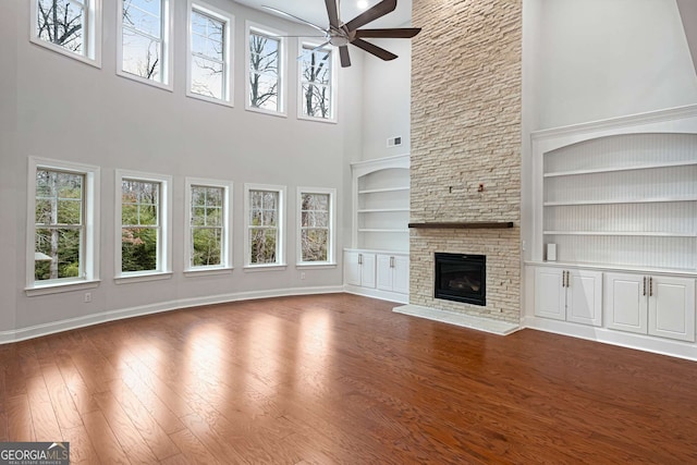 unfurnished living room with dark wood finished floors, a stone fireplace, a ceiling fan, and baseboards