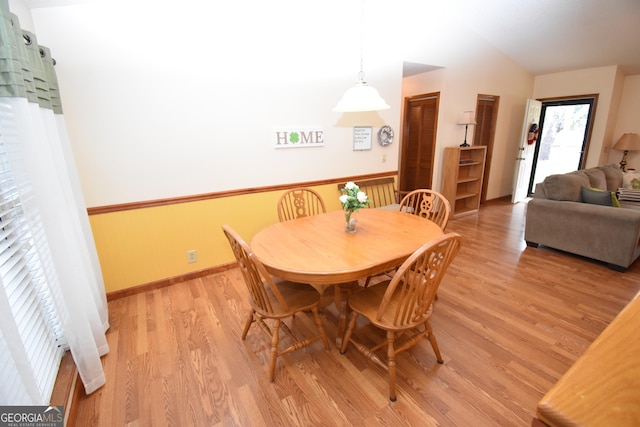 dining space with light wood-type flooring, baseboards, and vaulted ceiling