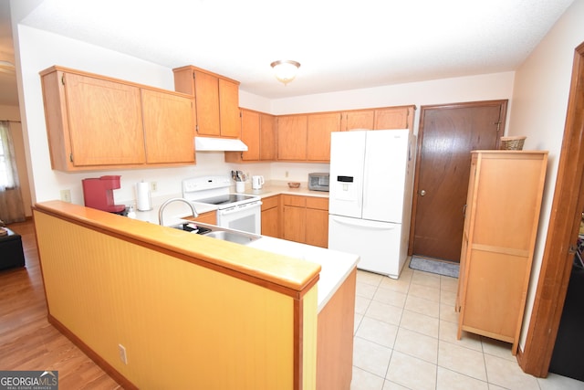 kitchen with under cabinet range hood, a sink, white appliances, a peninsula, and light countertops