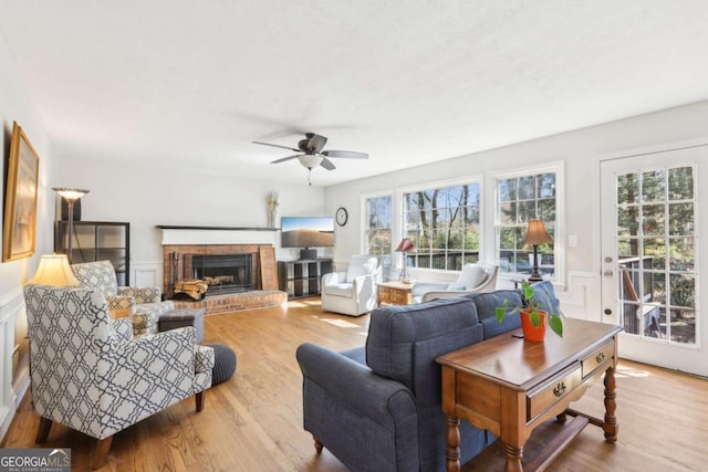 living area with wood finished floors, a wainscoted wall, a fireplace, ceiling fan, and a decorative wall