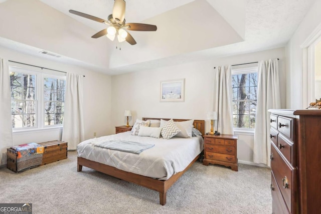 bedroom with a ceiling fan, a tray ceiling, light colored carpet, and visible vents