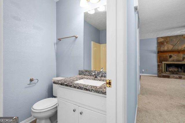 bathroom featuring a stone fireplace, toilet, vanity, and baseboards