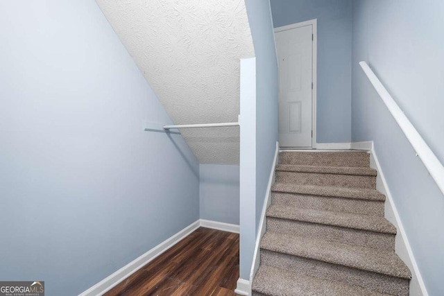 stairway featuring baseboards, a textured ceiling, wood finished floors, and vaulted ceiling