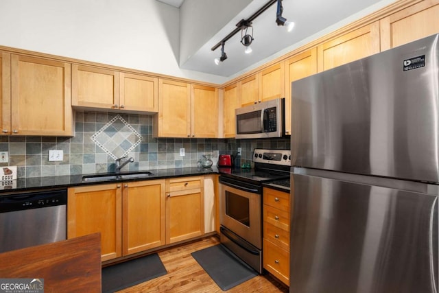 kitchen with dark stone countertops, light wood finished floors, a sink, decorative backsplash, and appliances with stainless steel finishes