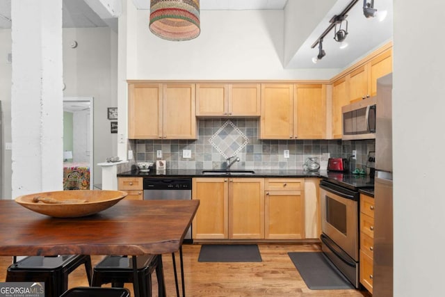 kitchen with a sink, appliances with stainless steel finishes, dark countertops, light wood-type flooring, and backsplash