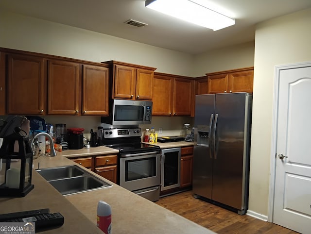 kitchen with visible vents, brown cabinets, a sink, stainless steel appliances, and dark wood-style flooring