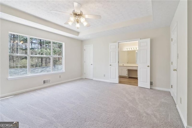 unfurnished bedroom with baseboards, visible vents, ensuite bathroom, a raised ceiling, and carpet flooring