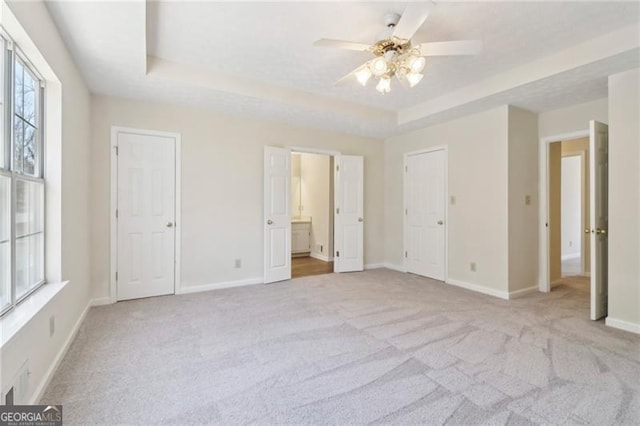 unfurnished bedroom featuring visible vents, a tray ceiling, connected bathroom, carpet, and baseboards