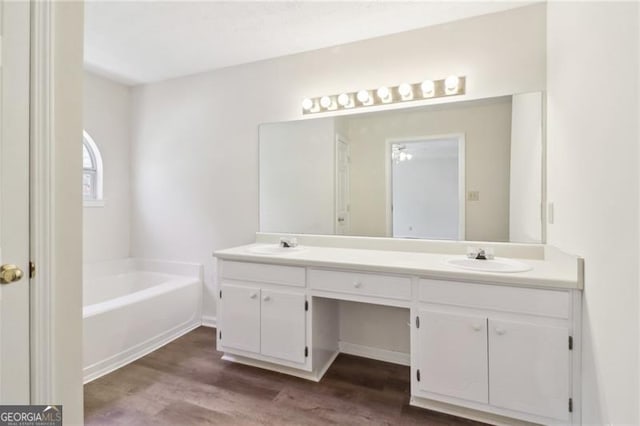 full bath featuring double vanity, a bath, wood finished floors, and a sink