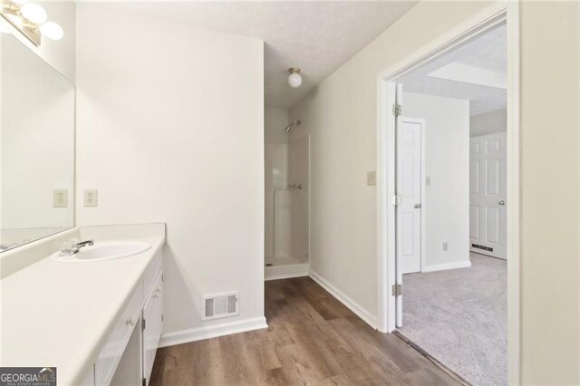 full bath featuring visible vents, wood finished floors, baseboards, walk in shower, and vanity