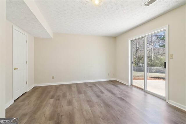 spare room featuring visible vents, baseboards, a textured ceiling, and wood finished floors