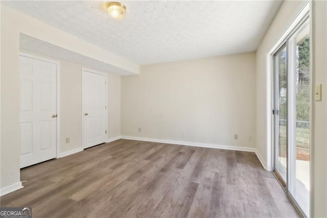 unfurnished bedroom with baseboards, wood finished floors, a textured ceiling, and access to exterior