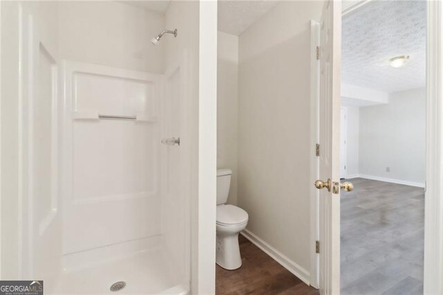 full bathroom featuring wood finished floors, baseboards, a shower stall, a textured ceiling, and toilet