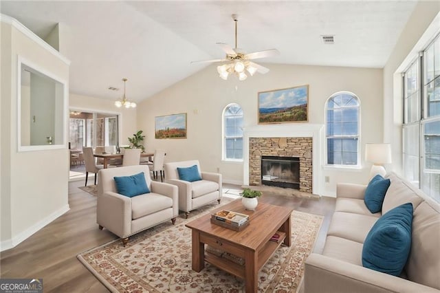 living room featuring wood finished floors, visible vents, baseboards, lofted ceiling, and a stone fireplace