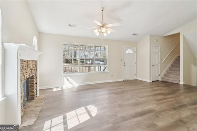 unfurnished living room featuring a stone fireplace, stairway, wood finished floors, and visible vents