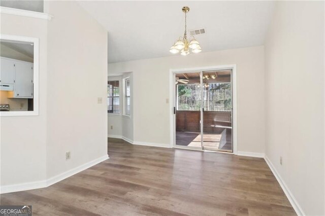 unfurnished dining area featuring a chandelier, visible vents, baseboards, and wood finished floors