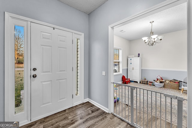 foyer with a chandelier, a textured ceiling, baseboards, and wood finished floors