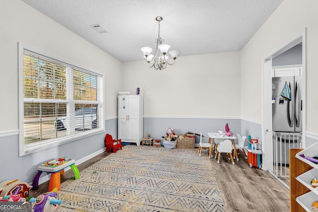 rec room with visible vents, a textured ceiling, an inviting chandelier, and wood finished floors