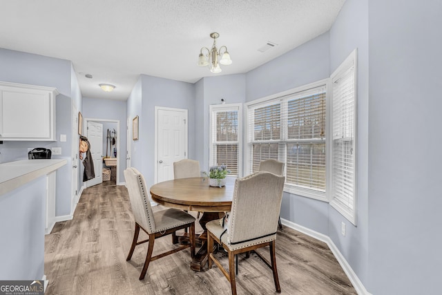 dining area with light wood-type flooring, visible vents, a notable chandelier, a textured ceiling, and baseboards