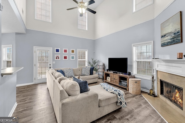 living area featuring a ceiling fan, visible vents, wood finished floors, baseboards, and a high end fireplace