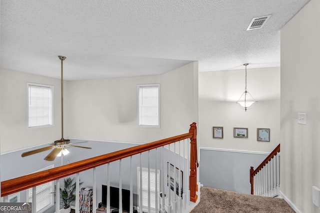 corridor featuring an upstairs landing, visible vents, and a textured ceiling