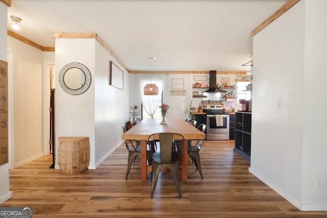 dining room with a textured ceiling, crown molding, baseboards, and wood finished floors