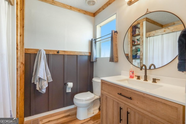 bathroom with vanity, toilet, wood finished floors, and ornamental molding