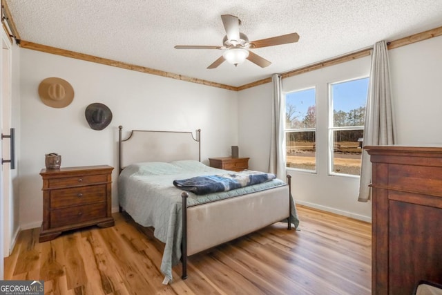 bedroom featuring ceiling fan, a textured ceiling, light wood-style flooring, and crown molding