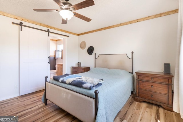 bedroom featuring light wood finished floors, ceiling fan, a textured ceiling, a barn door, and connected bathroom