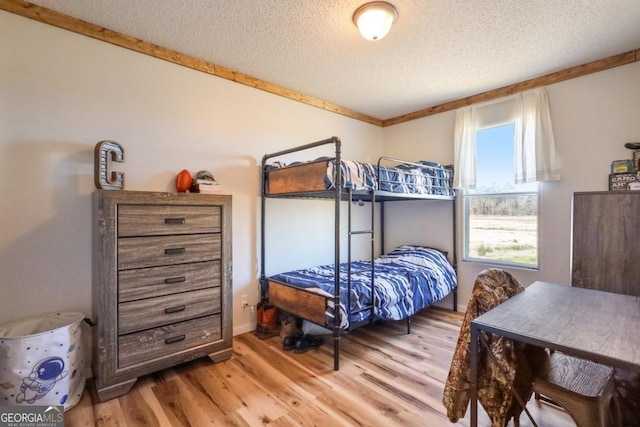 bedroom with a textured ceiling, light wood-style flooring, and ornamental molding