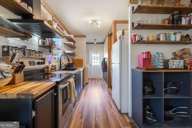 kitchen with open shelves, freestanding refrigerator, a sink, stainless steel range with electric cooktop, and under cabinet range hood