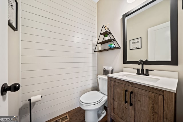 half bath with visible vents, toilet, wood finished floors, and vanity