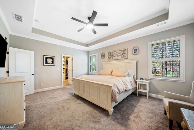 bedroom with a tray ceiling, light colored carpet, visible vents, and baseboards