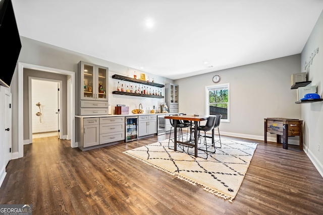 dining room with beverage cooler, dark wood-style floors, a bar, and baseboards