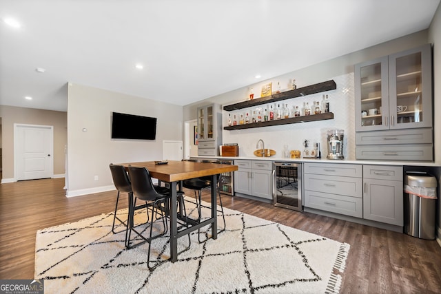 dining space featuring wet bar, dark wood-style floors, beverage cooler, and baseboards