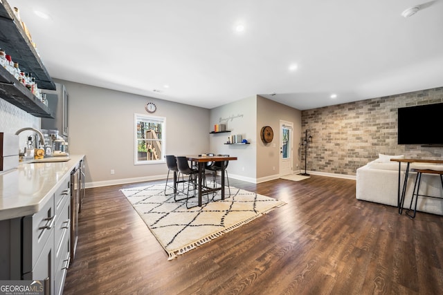 dining space with bar area, dark wood-style floors, recessed lighting, brick wall, and baseboards