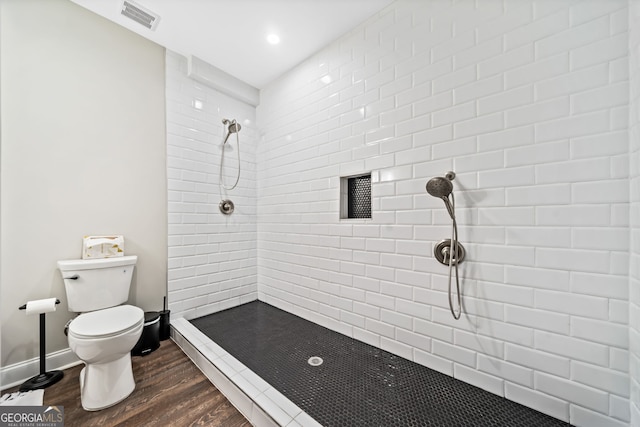 bathroom featuring visible vents, baseboards, toilet, a tile shower, and wood finished floors