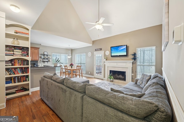 living room featuring wood finished floors, baseboards, high vaulted ceiling, a fireplace, and ceiling fan