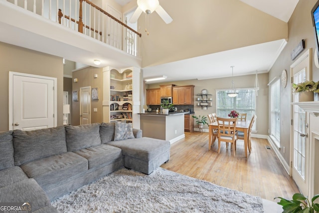 living room with light wood-style flooring, baseboards, a high ceiling, and a ceiling fan