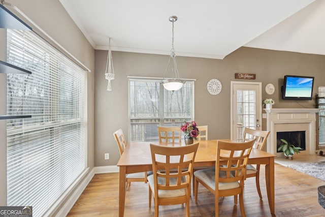 dining area featuring baseboards, crown molding, a fireplace, and light wood finished floors