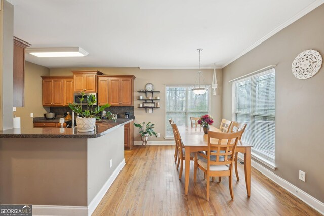 kitchen with light wood finished floors, stainless steel microwave, backsplash, baseboards, and brown cabinetry