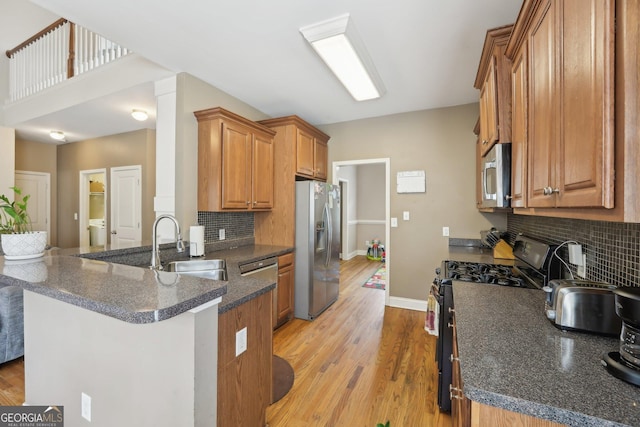 kitchen featuring appliances with stainless steel finishes, a peninsula, light wood-style floors, brown cabinetry, and a sink