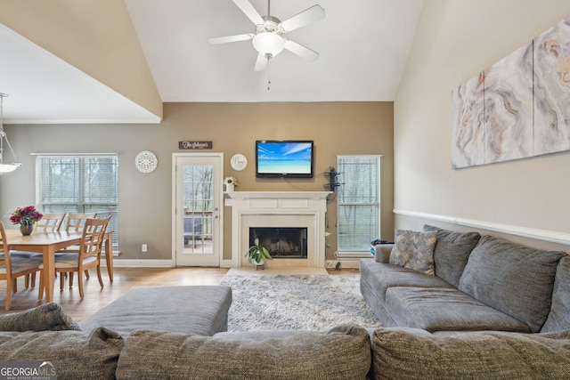 living area with a high end fireplace, wood finished floors, ceiling fan, and vaulted ceiling