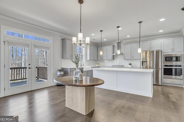 kitchen with ornamental molding, gray cabinets, a center island, stainless steel appliances, and wall chimney range hood