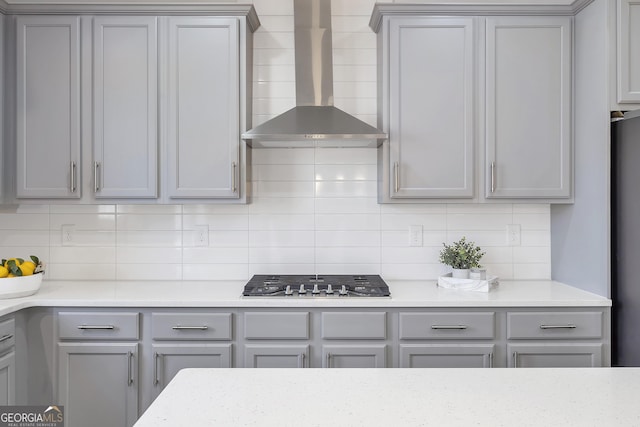 kitchen with gray cabinets, light countertops, stainless steel gas stovetop, wall chimney range hood, and tasteful backsplash