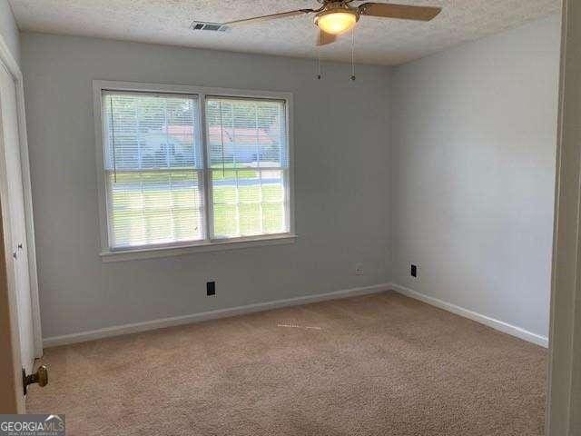 carpeted spare room with a ceiling fan, baseboards, visible vents, and a textured ceiling