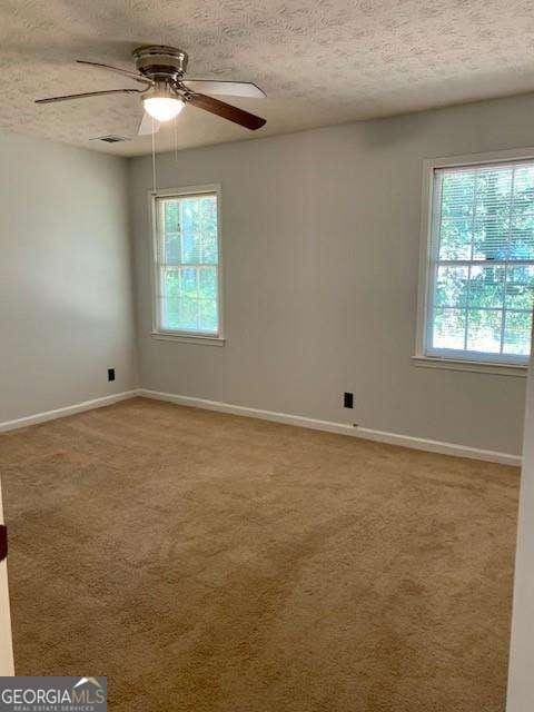 empty room with carpet flooring, a healthy amount of sunlight, a textured ceiling, and visible vents