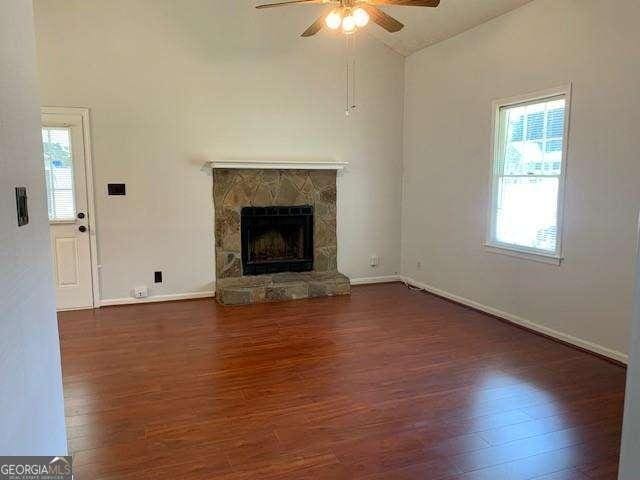 unfurnished living room with wood finished floors, baseboards, a ceiling fan, a stone fireplace, and vaulted ceiling