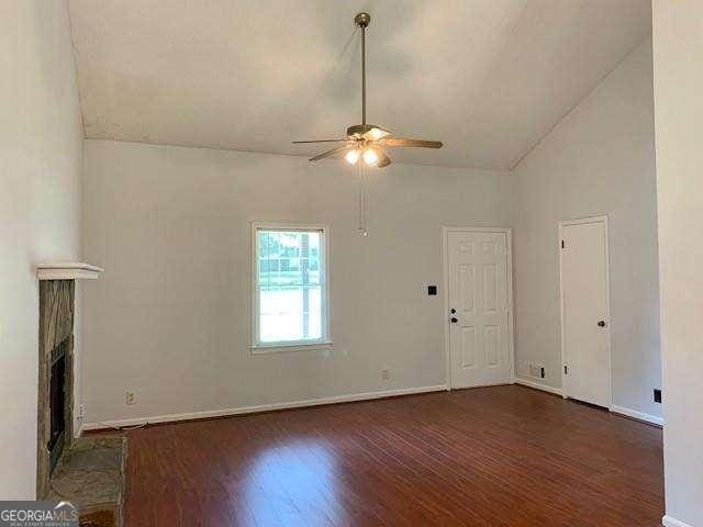 unfurnished living room with wood finished floors, baseboards, high vaulted ceiling, a fireplace, and ceiling fan