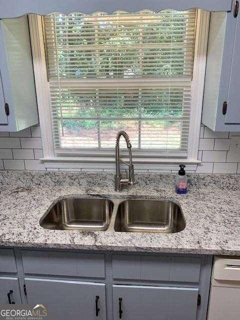 interior details featuring light stone counters, decorative backsplash, dishwasher, and a sink